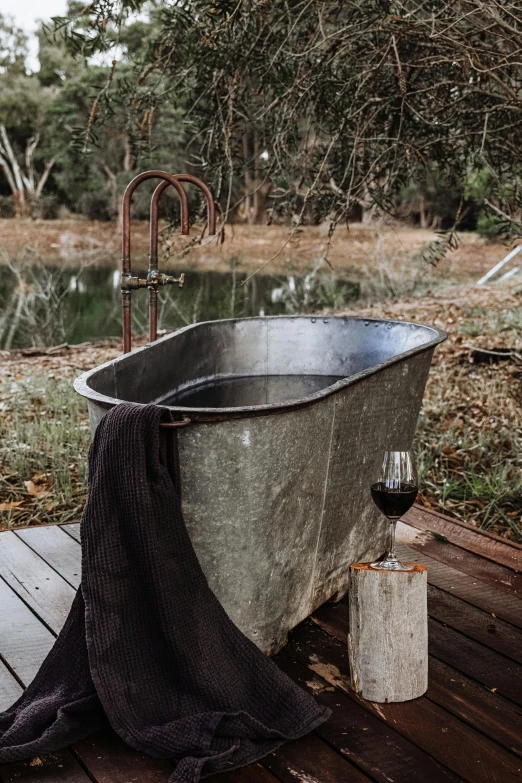 a bath tub sitting on top of a wooden deck, by Jessie Algie, river of wine, stainless steal, camp, charcoal and champagne