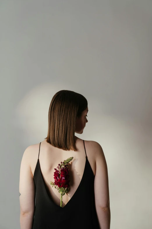 a woman in a black dress with a flower on her back, a tattoo, inspired by Elsa Bleda, pexels contest winner, hyperrealism, fleshy botanical, cut out, looking out, kailee mandel