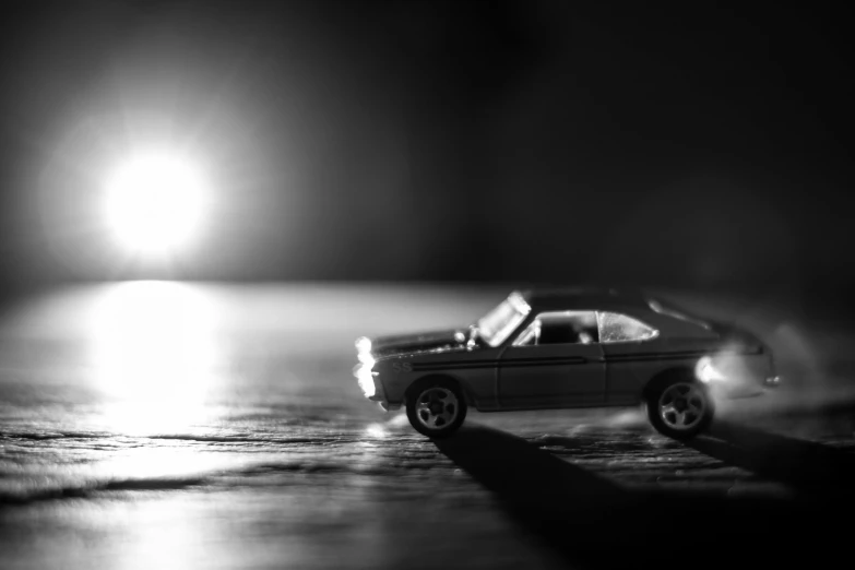 a toy car sitting on top of a wooden table, a black and white photo, by Dariusz Zawadzki, unsplash, photorealism, light trail, hotwheels, summer night, run down