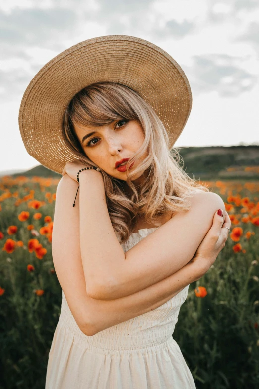 a woman wearing a hat standing in a field of flowers, a colorized photo, trending on pexels, blonde and attractive features, poppy, center parted bangs, casual pose