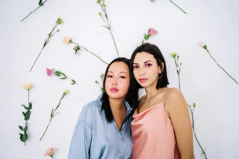 a couple of women standing next to each other, inspired by Wang Duo, trending on pexels, flowers in background, olive skin color, in front of white back drop, pink and blue