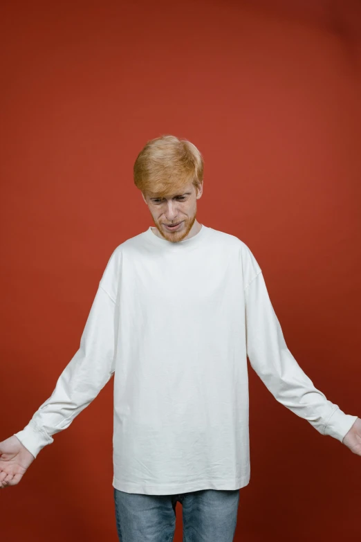 a man standing in front of a red wall, an album cover, wearing a white sweater, ginger hair, wearing a white hospital gown, on a gray background