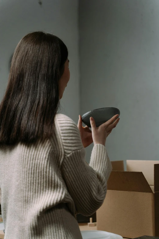 a woman standing in a room holding a bowl, trending on pexels, delivering parsel box, home video footage, inspect in inventory image, woman is curved