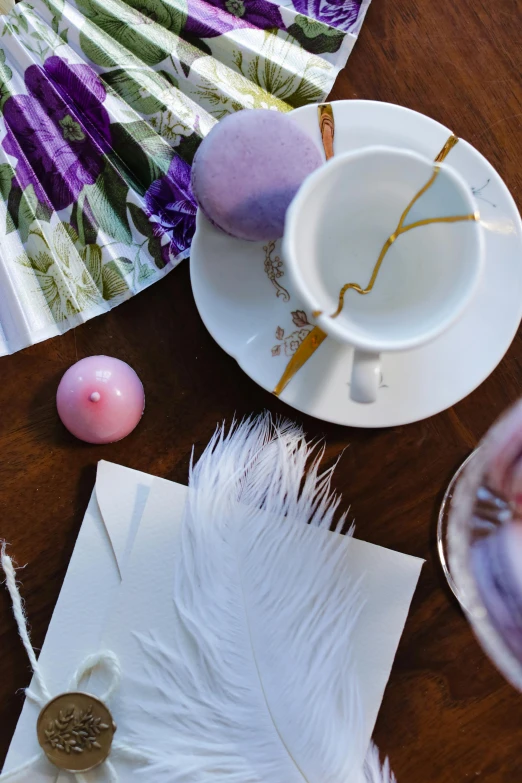 a table topped with a cup of coffee and a fan, inspired by Rudolf von Alt, pexels contest winner, process art, purple feathers, ornate egg, candy decorations, detail shot