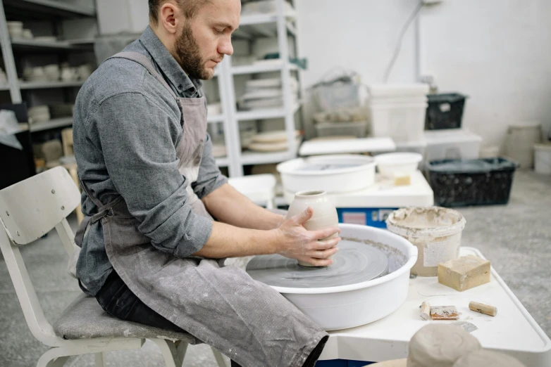 a man is making a bowl out of clay, a portrait, trending on unsplash, arbeitsrat für kunst, full body image, made in tones of white and grey, foreground background, plating