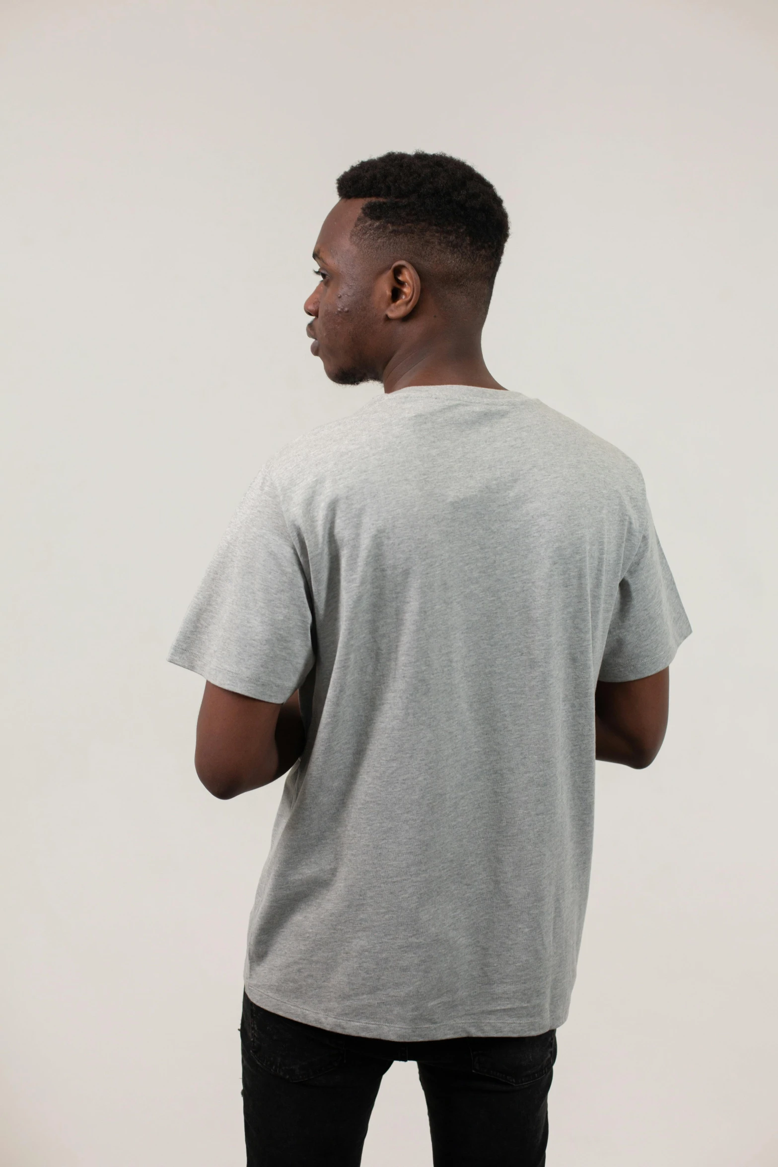 a man standing in front of a white wall, gray shirt, back view. nuri iyem, full product shot, wearing a t-shirt