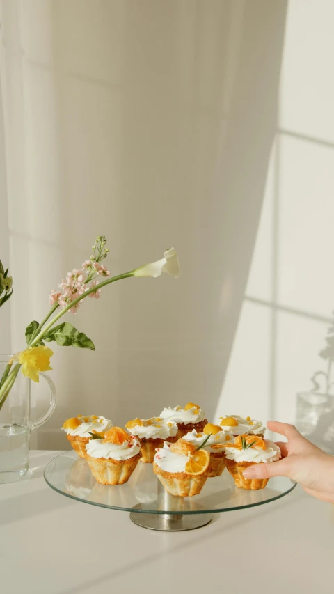 a woman holding a plate with cupcakes on it, a still life, trending on pexels, daffodils, white marble interior photograph, orange yellow ethereal, low quality photo