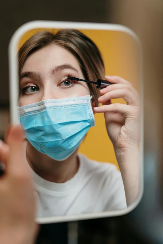 a woman putting on a mask in front of a mirror, a picture, trending on pexels, surgical gear, large friendly eyes, yellow makeup, photo of young woman