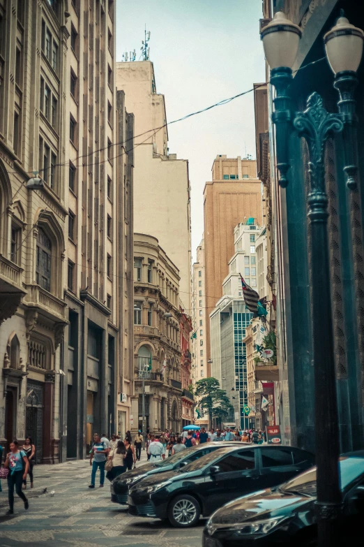 a group of people walking down a street next to tall buildings, a picture, by Felipe Seade, pexels contest winner, art nouveau, colonial era street, photograph of the city street, brazilian, street of teal stone