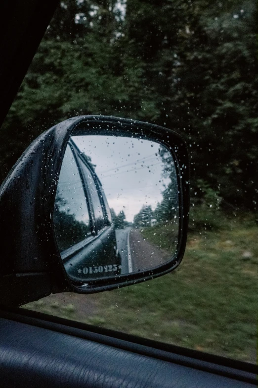 a rear view mirror on the side of a car, it's raining outside, paul barson, photo from behind, van