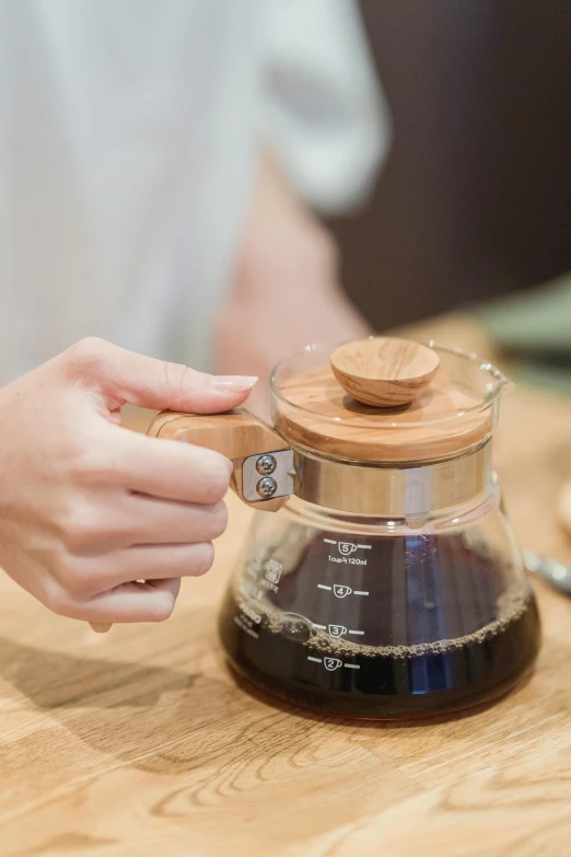 a person preparing a cup of coffee on a table, bamboo wood, short spout, detailed product image, back