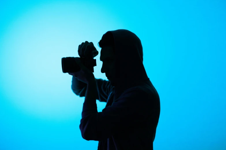 a person holding a camera in front of a blue background, inspired by Elsa Bleda, silhouette of man, posing for a picture, high res photograph, avatar image