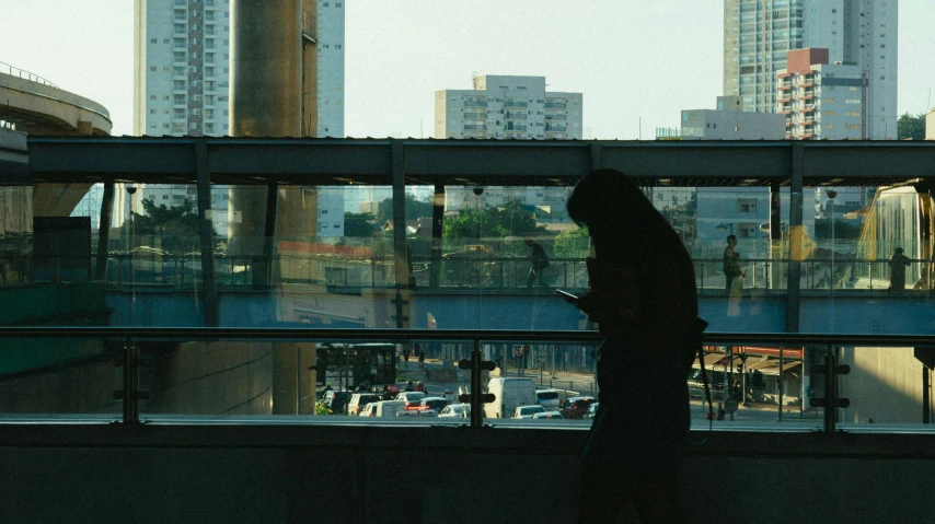 a person standing in front of a window looking at a cell phone, inspired by Elsa Bleda, realism, sao paulo, **cinematic, koyaanisqatsi, ignant