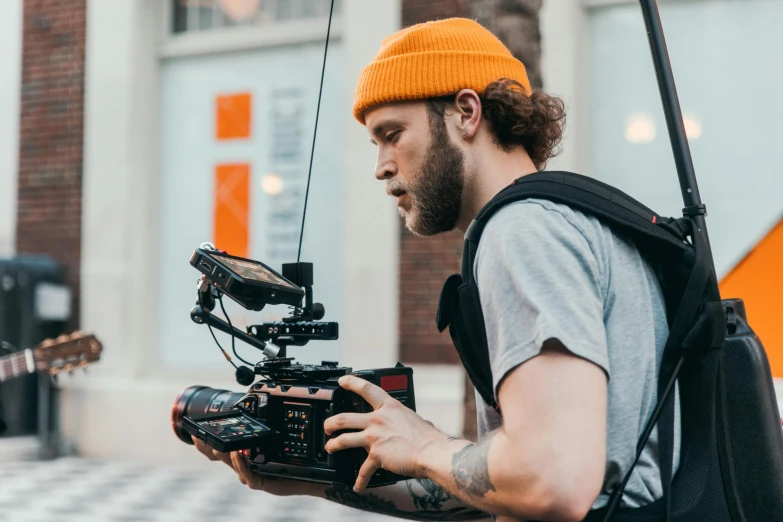 a man holding a camera in front of a building, trending on pexels, realism, action sports, performing a music video, crane shot, looking the camera