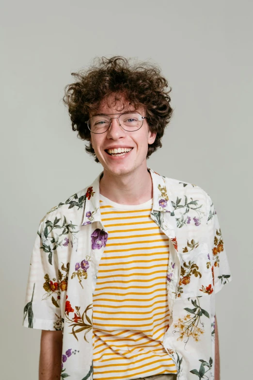 a man with curly hair wearing glasses and a floral shirt, by Jacob Toorenvliet, wearing stripe shirt, teenager, joyful smirk, in simple background