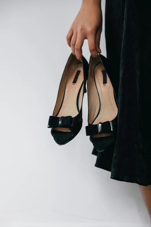 a woman holding a pair of black shoes, by Barron Storey, trending on unsplash, black tie, wide skirts, y2k”, made of glazed