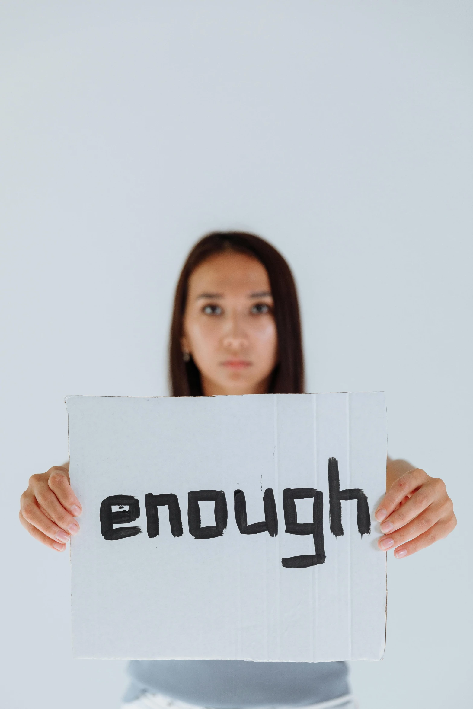 a woman holding a sign that says enough, unsplash, realism, pokimane, depressing image, close - up studio photo, background image