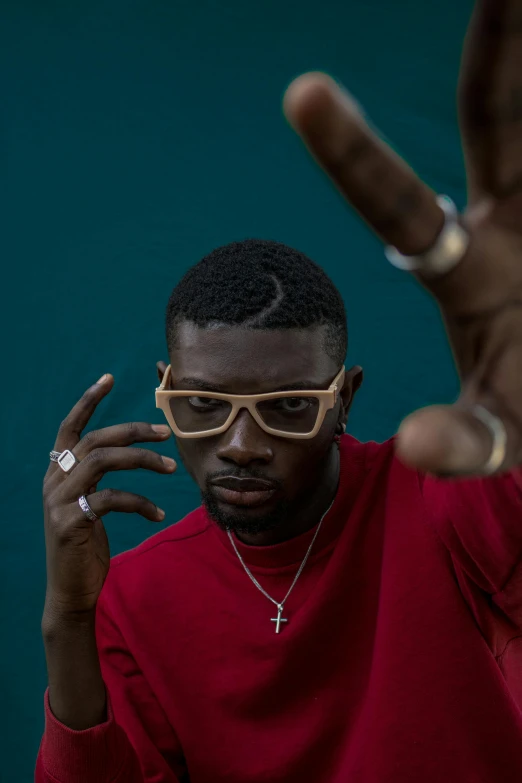 a man in a red shirt is making a peace sign, an album cover, inspired by Paul Georges, trending on pexels, gucci glasses, riyahd cassiem, mid shot portrait, shot with sony alpha