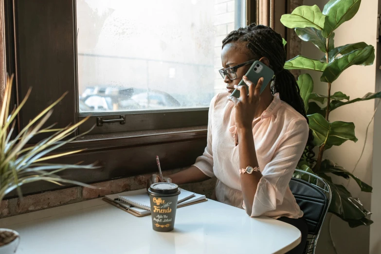 a woman sitting at a table talking on a cell phone, pexels contest winner, nerdy black girl super hero, sitting on a mocha-colored table, customers, african canadian