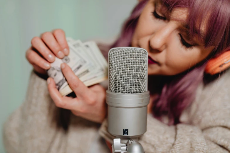 a woman holding money in front of a microphone, trending on pexels, realism, 🦩🪐🐞👩🏻🦳, dream recording, soft and detailed, professionally done