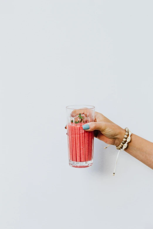 a woman's hand holding a glass of watermelon juice, by Carey Morris, pexels, minimalism, tall thin, straw, raspberry, vanilla smoothie explosion