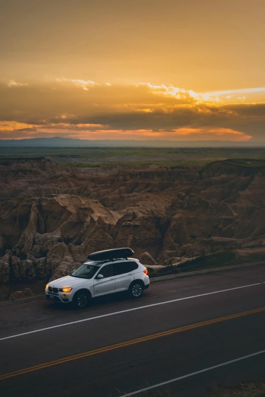 a white car driving down a road at sunset, by Andrew Domachowski, pexels contest winner, badlands, square, over a cliff, with a roof rack