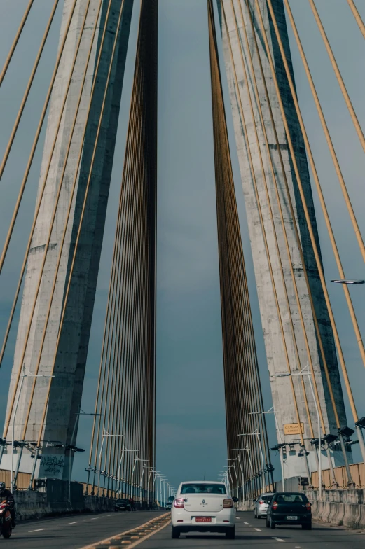 a couple of cars driving across a bridge, an album cover, by Joze Ciuha, pexels contest winner, postminimalism, gold cables, tall thin build, view from bottom, twin towers