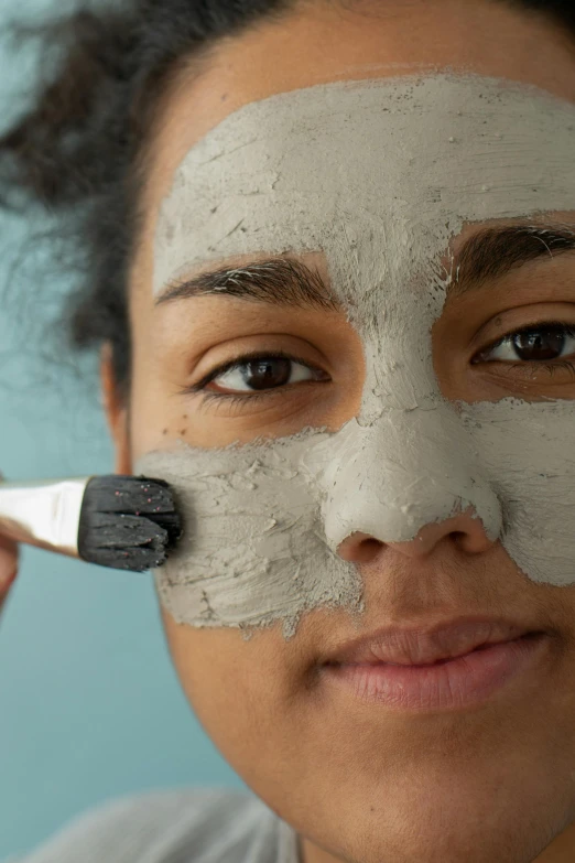 a woman is putting a mask on her face, trending on pexels, square facial structure, hard clay, grey, 5 7 9