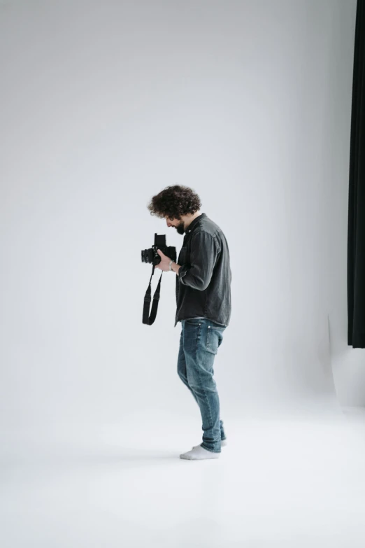 a man standing in a studio holding a camera, facing away from the camera, zac retz, interacting and posing, in a white room