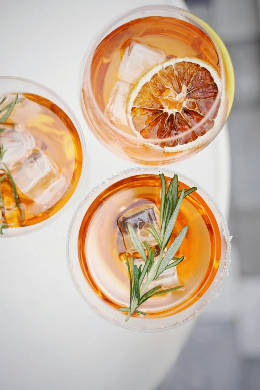 three glasses filled with drinks sitting on top of a table, by Carey Morris, trending on pexels, renaissance, orange halo, mediterranean, manuka, square