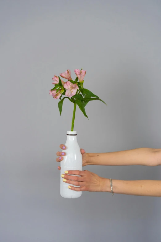 a woman holding a white vase with pink flowers in it, unsplash, upcycled, holding a bottle of arak, 3/4 front view, enamel