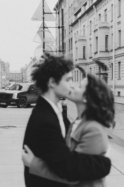 a man and woman kissing on a city street, a black and white photo, timothee chalamet, saint petersburg, profile image, curly haired