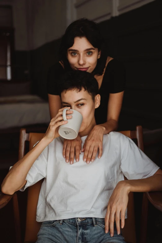 a man sitting in a chair next to a woman, by Cosmo Alexander, trending on pexels, portrait androgynous girl, coffee cup, sisters, asian female