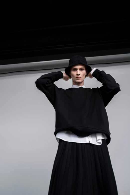 a man standing with his hands on his head, an album cover, unsplash, bauhaus, baggy clothing and hat, yohji yamamoto, genderless, black wool sweater