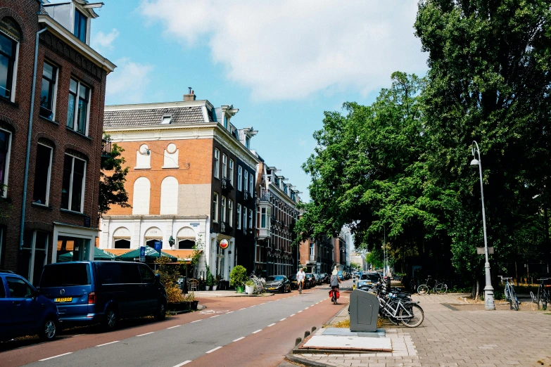 a street lined with parked cars next to tall buildings, by Jan Tengnagel, delft, trees around, background image, sunny day time