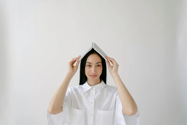 a woman holding a book over her head, an album cover, inspired by Fei Danxu, unsplash, wearing a white button up shirt, wearing pointed hoods, simple structure, instagram picture