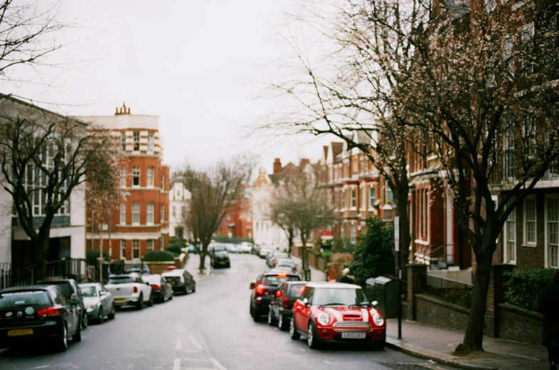 a street filled with lots of parked cars, inspired by Thomas Struth, unsplash, red mini cooper s, victorian london, maple trees along street, medium format film photography