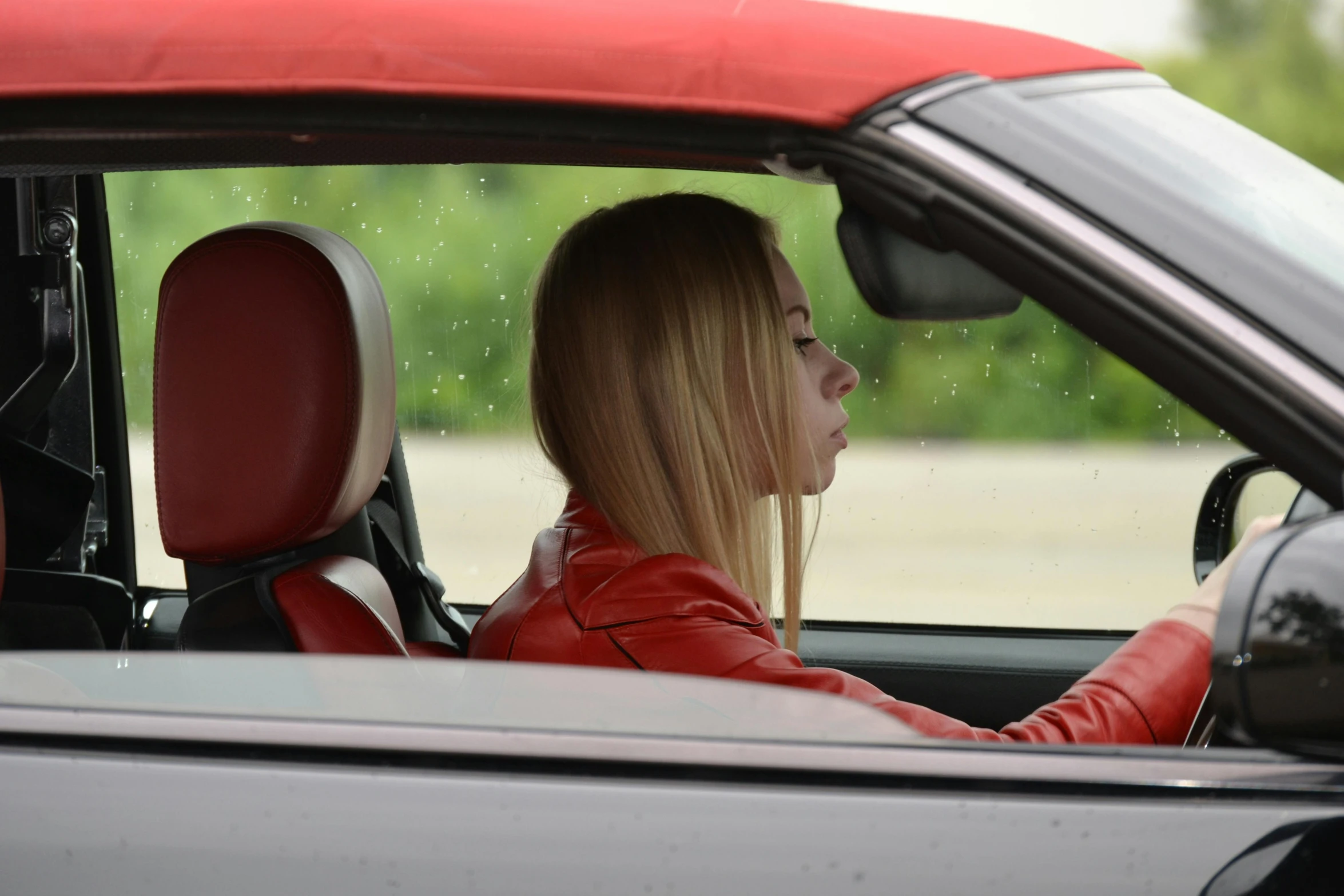 a woman sitting in the driver's seat of a car, a picture, sydney sweeney, red leather jacket, side profile artwork, topdown