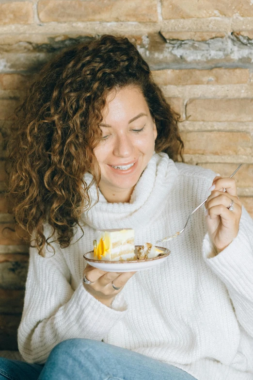 a woman sitting in front of a brick wall eating a piece of cake, pexels contest winner, renaissance, wavy hair yellow theme, wearing a white sweater, people inside eating meals, profile image