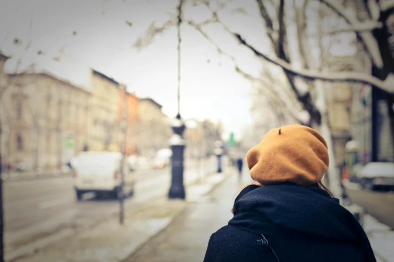 a person is walking down a city street, by Lucia Peka, trending on pexels, wearing beanie, looking from behind, peaceful day, childhood friend
