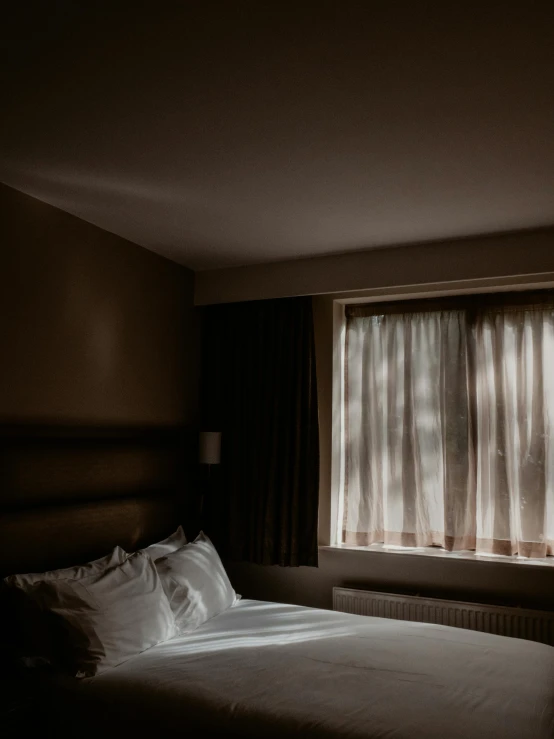 a bed sitting in a bedroom next to a window, a portrait, inspired by Elsa Bleda, unsplash, dramatic lighting - n 9, hotel room, taken in the late 2010s, brown