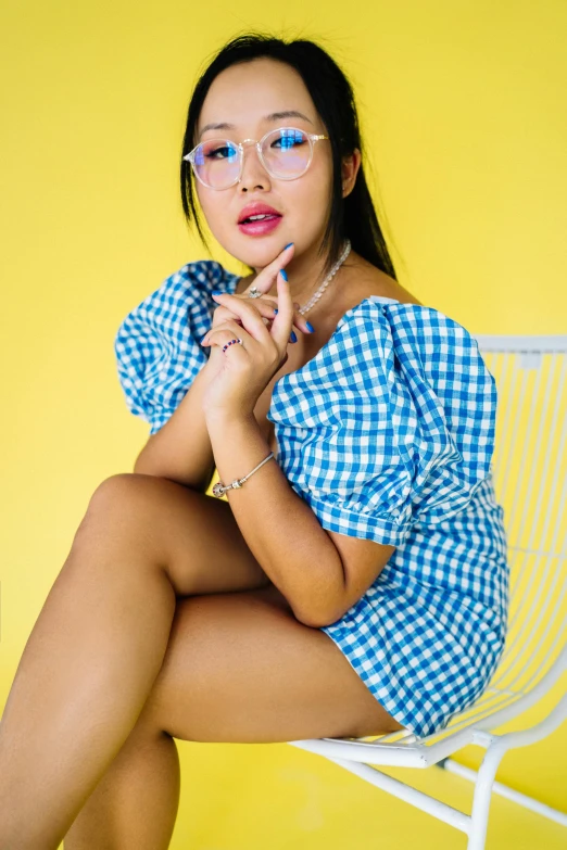 a woman sitting on top of a white chair, inspired by helen huang, trending on pexels, pop art, blue checkerboard dress, small square glasses, thighs close up, young asian woman