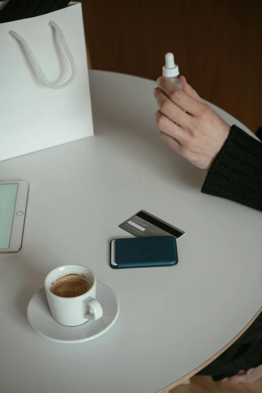 a person sitting at a table with a cup of coffee, holding a battery, product image, curated collections, square