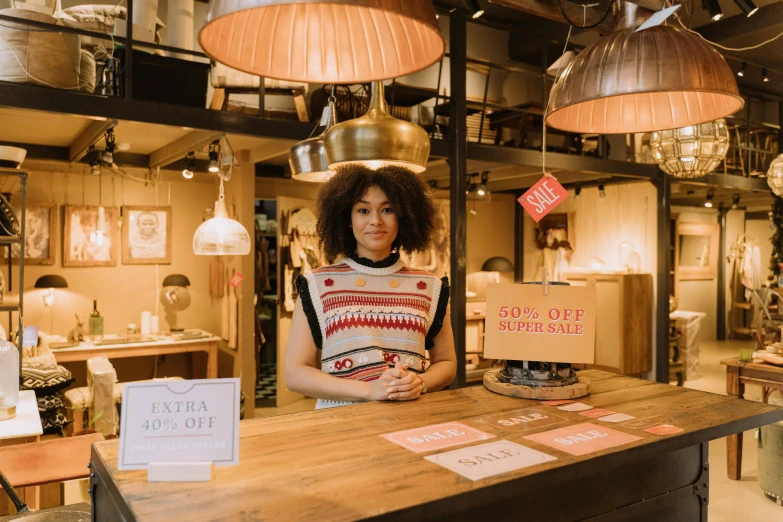 a woman standing at a counter in a store, pexels contest winner, furniture around, tessa thompson, warm street lights store front, emma bridgewater and paperchase