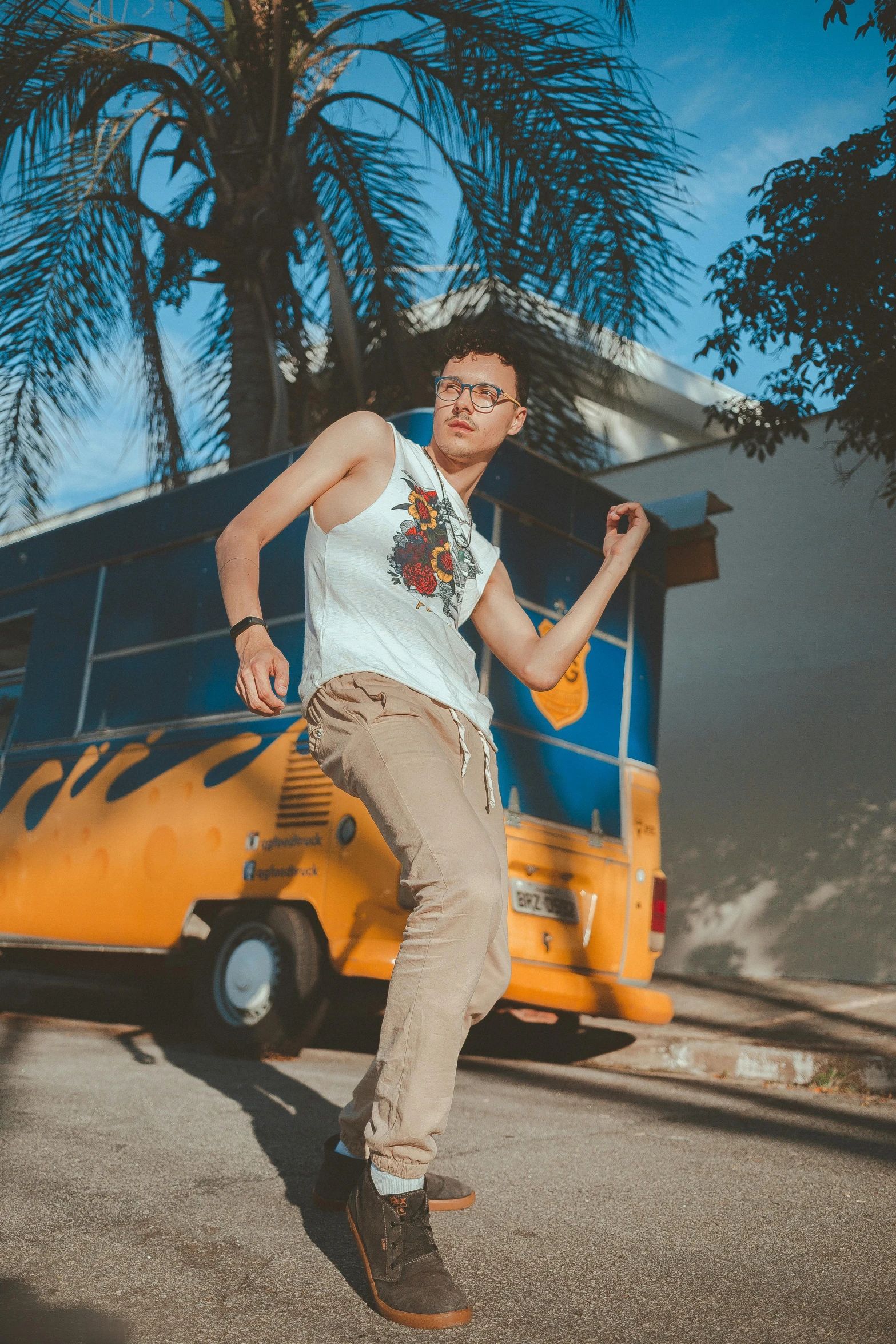 a man riding a skateboard down a street next to a yellow bus, an album cover, pexels contest winner, white! tank top with a print, jewish young man with glasses, model posing, asian male