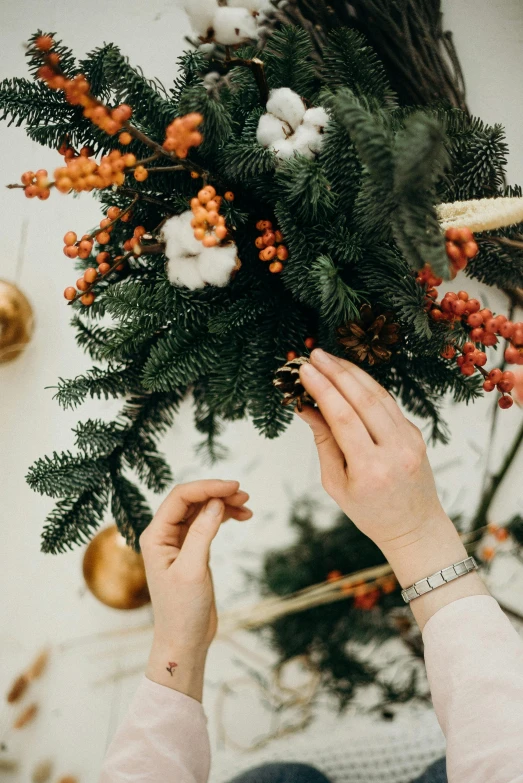 a woman placing a wreath on top of a christmas tree, by Julia Pishtar, trending on pexels, baroque, made of flowers and berries, golden details!, how-to, hanging