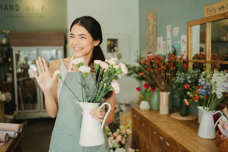 a woman standing in a flower shop holding a vase of flowers, pexels contest winner, waving, wearing an apron, low quality photo, trending on