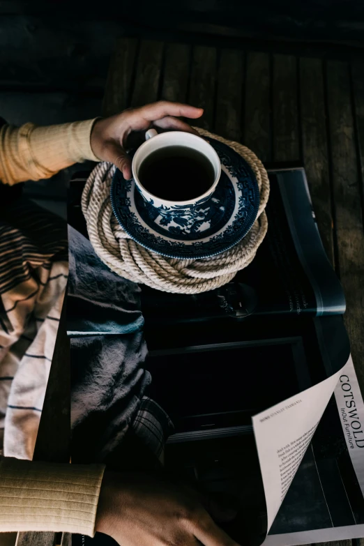 a person sitting at a table with a cup of coffee, wearing dark maritime clothing, rope, instagram picture, unsplash photography