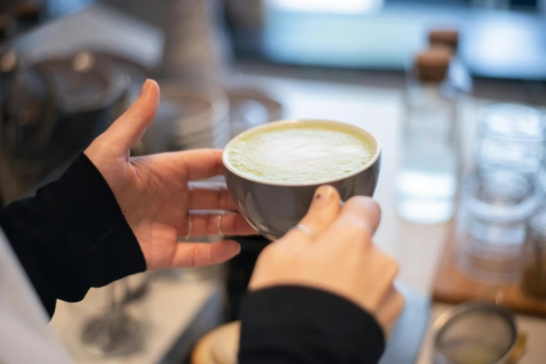 a close up of a person holding a cup of coffee, full of greenish liquid, latte art, amanda lilleston, lachlan bailey