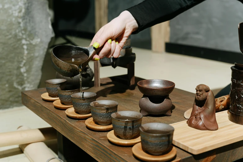 a wooden table topped with bowls and cups, inspired by Miyagawa Chōshun, trending on unsplash, mingei, pouring, partially cupping her hands, made of tar, aussie baristas